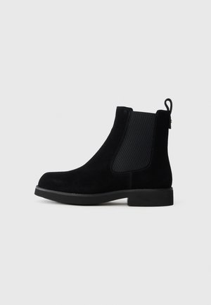 Botine Chelsea din suede negru, cu panouri laterale elastice, un tab de tragere și o talpă din cauciuc plat. Prezintă un design elegant cu vârf rotunjit.