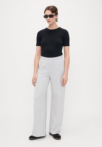 Μαύρο κοντομάνικο εφαρμοστό μπλουζάκι σε συνδυασμό με ανοιχτό γκρι υφασμάτινα παντελόνια με φαρδιά γραμμή. Το μοντέλο φοράει μαύρα γυαλιά ηλίου και μαύρες επίπεδες παπούτσια.