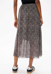 Jupe maxi plissée à motifs léopard avec une texture fluide et transparente, dotée d'une taille noire et portée avec des baskets noir et blanc.