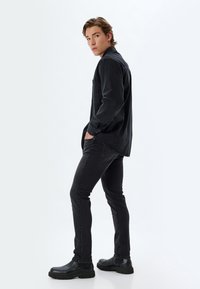 Camisa de mezclilla negra con cuello, bolsillo en el pecho y mangas largas; combinada con jeans negros ajustados y botas de tobillo negras. Textura suave.