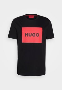 T-shirt nero a maniche corte con un rettangolo rosso sul petto che presenta la parola "HUGO" in grassetto lettere nere.