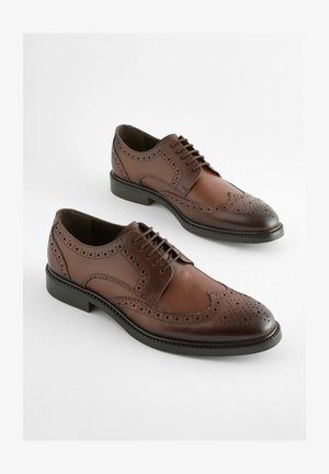 Chaussures derby en cuir marron avec un design brogue, bout pointu et semelle en caoutchouc plate. Perforations intriquées le long des bords.