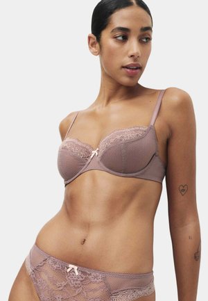 Woman wearing matching mauve lace bra and panties, posing with her head turned to the side against a plain light background.