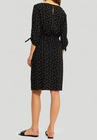 Robe noire à pois avec des manches trois-quarts, taille cintrée et un détail en ouverture dans le dos. Tissu doux avec une coupe décontractée.