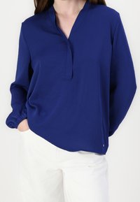Navyblaue Bluse mit langen Ärmeln, V-Ausschnitt und elastischen Bündchen. Weicher Stoff, lockere Passform und seitliche Schlitzdetails am Saum.