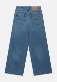 Ανοιχτό μπλε παντελόνι από τζιν με φαρδύ πόδι. Διαθέτει καφέ δερμάτινη ταμπέλα στη μέση και δύο πίσω τσέπες με λεπτομέρειες ραφής.