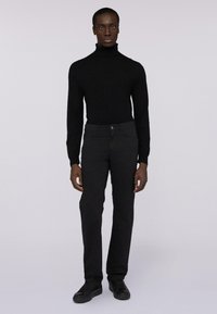 Maglione nero a collo alto realizzato in un materiale a maglia morbido, abbinato a pantaloni neri slim-fit. La texture è uniforme, con chiusura frontale a bottoni.