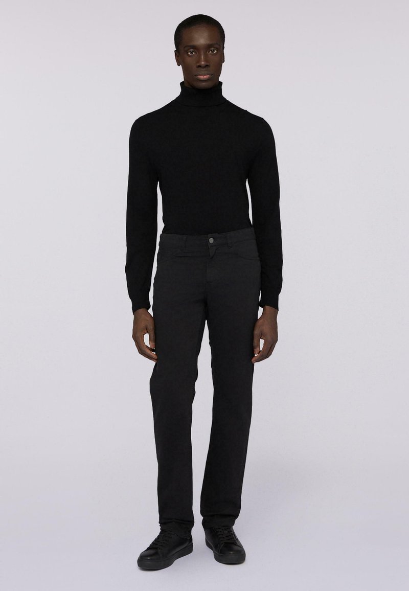 Maglione nero a collo alto realizzato in un materiale a maglia morbido, abbinato a pantaloni neri slim-fit. La texture è uniforme, con chiusura frontale a bottoni.