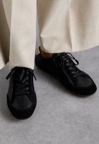 Sneaker neri caratterizzati da un mix di pelle liscia e morbida suede, con punte arrotondate, stringhe piatte e un piccolo dettaglio beige sul tallone.