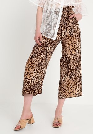 Mujer con pantalones anchos cropped con estampado de leopardo, blusa blanca floral transparente y sandalias beige de tacón con dedos descubiertos.