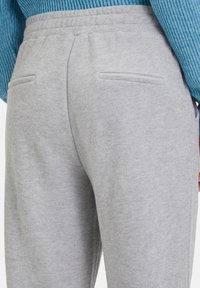 Grijze sweatpants met een zachte textuur, elastische tailleband en twee achterzakken. Het materiaal lijkt ademend en casual.