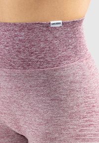 Leggings sportivi a vita alta in un tessuto bordeaux testurizzato, con un'etichetta del marchio in vita e un design senza cuciture.