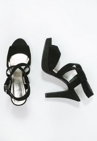 Svarta högklackade sandaler med en mjuk mockakänsla, öppen tå, korsade remmar och en metallisk sula; upphöjd plattform och stilettklack.