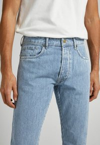 Randiga blå denimjeans med en figurnära design, med vertikala vita ränder, standardfickor och stängning med metallknapp.