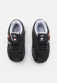 Svarta sneakers med mesh och syntetmaterial, vita sulor, Hello Kitty-detaljer och svarta skosnören. Toppsikt som visar design och logotyp.