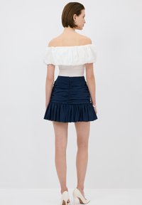 Off-shoulder vit topp med puffärmar; marinblå volangkjol; texturerad tyg; figursydd design; dragkedjestängning bak.