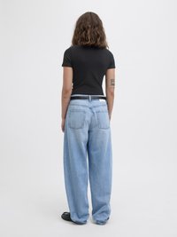 Schwarzes kurzärmliges Oberteil, hellblaue übergroße Denim-Jeans mit zwei Gesäßtaschen, stehend auf schwarzen Schuhen vor einem weißen Hintergrund.