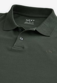 Polo de color verde oscuro con cuello acanalado, tapeta de dos botones y logotipo bordado. Fabricado con tejido de algodón texturizado. Corte regular.