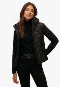 Veste noire en couches avec un gilet matelassé et des manches ajustées. Présente un col haut, des textures contrastantes et une boucle de ceinture en argent.