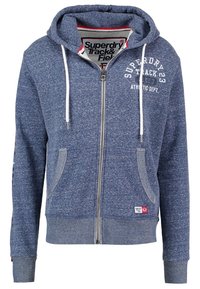 Kapuzensweatshirt mit Reißverschluss in Marineblau, mit melierter Textur, weißen Kordeln und einem grafischen Aufdruck auf der Brust. Mit seitlichen Taschen.