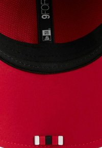 Rote Kappe mit schwarzem Schirm, ausgestattet mit einem Netz-Innenfutter, einem Etikett mit der Aufschrift "9FOR" und einem dekorativen Akzent aus roten, schwarzen und weißen Quadraten.