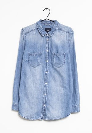 Light blue denim long-sleeve button-up shirt with two chest pockets hanging on a black hanger against a white background.