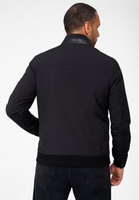 Schwarze Bomberjacke mit glatter Textur, ausgestattet mit einem Lederkragen, gerippten Bündchen und Taillenbund, von hinten gesehen.