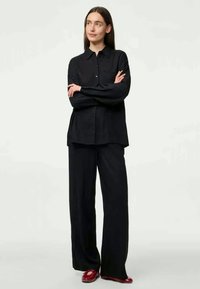 Must mustaga nööbiga särk, millel on krae, kombinatsioonis vaba lõikega mustade pükstega, mõlemad on valmistatud siledast kangast; riietust täiustavad punased kingad.