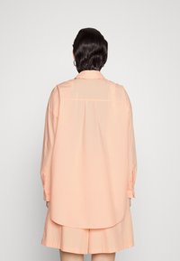 Peachfarvet oversized skjorte med en rygflag og knapmanchetter, parret med matchende shorts. Glat bomuldsstof, afslappet pasform.