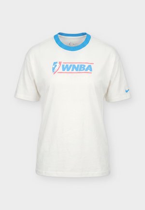 Mann trägt weißes WNBA-Logo-T-Shirt mit blauem Kragen und passenden weißen Sportshorts mit WNBA- und Nike-Logos, steht vor schlichtem Hintergrund.