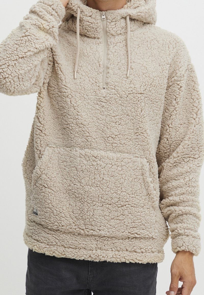 Beige fleece hættepullover med halvlynlås, kængurulomme og snoretræk i hætten. Tekstureret, hyggeligt stof med en afslappet pasform.