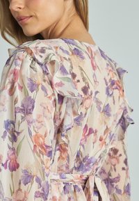 Vestido floral con mangas a rayas, hecho de tela ligera, con un estampado de flores moradas y rosas sobre un fondo crema.