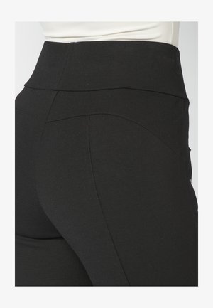 Mustad kõrge vöökohaga mustad retuusid, millel on sile tekstuur ja peidetud õmblused, pakkudes kehaürpivat siluetti.