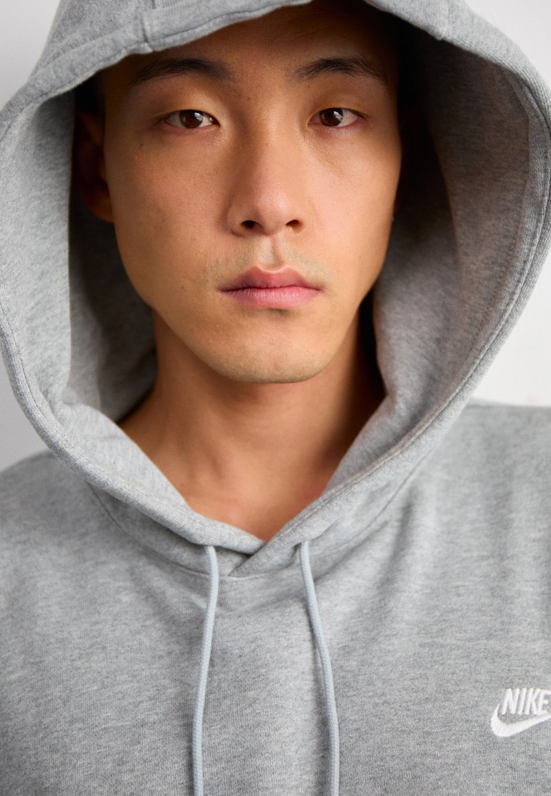 Szary hoodie wykonany z miękkiego materiału, z kapturem na sznurki i małym białym logo Nike na klatce piersiowej. Gładka tekstura i casualowy design.