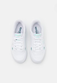Biele tenisky s perforovanou špičkou, šnúrkami a zelenými akcentmi. Na jazyku a päte branding "Reebok Classic" a "vegan". Hladký povrch.
