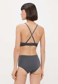 Sivý bralet s tenkými, prekríženými ramienkami a zapínaním na chrbte, spárovaný s vysokými sivými nohavičkami. Hladká textúra, minimalistický dizajn.