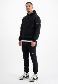 Zwarte sweatshirt en bijpassende joggers van een katoenmix. De hoodie heeft een voorvak en een merklogo. Sneakers hebben een patroonontwerp.