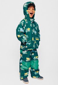 Giacca e pantaloni impermeabili verdi con motivi di veicoli da costruzione in giallo e azzurro chiaro. Con cappuccio, chiusura con zip e polsini elasticizzati.