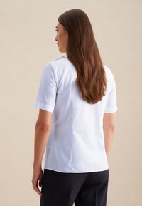 Blusa azzurra a maniche corte con una texture liscia e una linea dritta, dotata di una cucitura posteriore e polsini in contrasto.