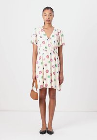 Floral print dress in cream with a V-neck and short flutter sleeves. Features colorful daisies and a waistline gather. Worn with black flats.