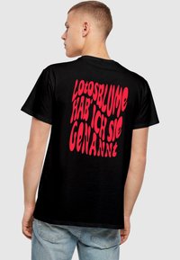 Sort t-shirt i bomuld med fed, uregelmæssig rød skrift på ryggen, der står "Lotosblume hab' ich sie genannt." Casual pasform.