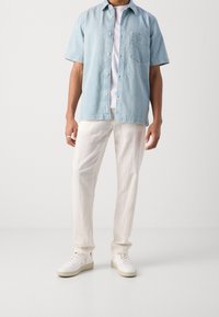 Ljusblå jeansskjorta med korta ärmar och en bröstficka, kombinerad med linnebyxor i krämfärg och vita sneakers. Enkel, avslappnad design.