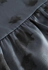 Grauer Stoff mit schwarzen abstrakten Mustern, der eine glatte Textur aufweist und versammelnde Details entlang der Naht hat, wodurch ein fließendes Aussehen entsteht.