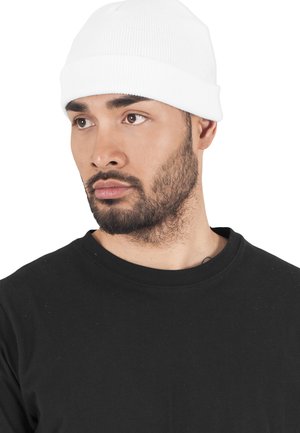 Valge ribaga beanie müts, mida kantakse musta särgiga. Müts on tihedalt peas, keeratud äär on olemas ja see on valmistatud tekstuurilisest kangast.