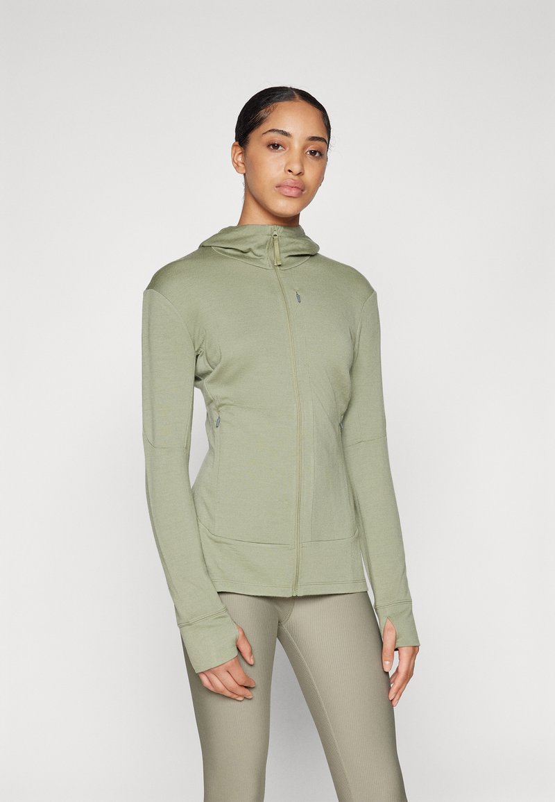 Sweatshirt verde com fecho éclair, de corte ajustado, apresentando uma gola alta, buracos para os polegares nas mangas e bolsos laterais. Tecido suave e texturizado.