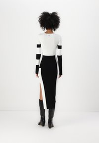 Kroppsnära klänning med svartvita vertikala ränder, sidospets, långa ärmar och rundad halsringning. Detaljer på baksidan.