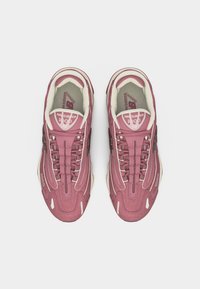 Ζευγάρι ροζ παπούτσια τρεξίματος New Balance 1100 με λευκές λεπτομέρειες, φωτογραφημένα από πάνω σε λευκό φόντο.