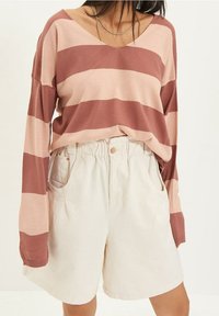 Pull rayé à manches longues dans des tons de rose et de brun doux, associé à un short taille haute beige, avec des poches latérales et une coupe décontractée.