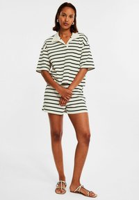 Randig kortärmad polotröja i krämfärg och svart, tillsammans med matchande shorts. Lätt tyg, avslappnad passform, med synliga sömsdetaljer.