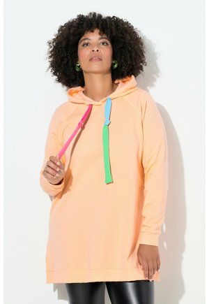 Persikofärgad hoodie med avslappnad passform, med flerfärgade dragsnöre (rosa, grön, blå) och långa ärmar, kombinerad med svarta leggings.